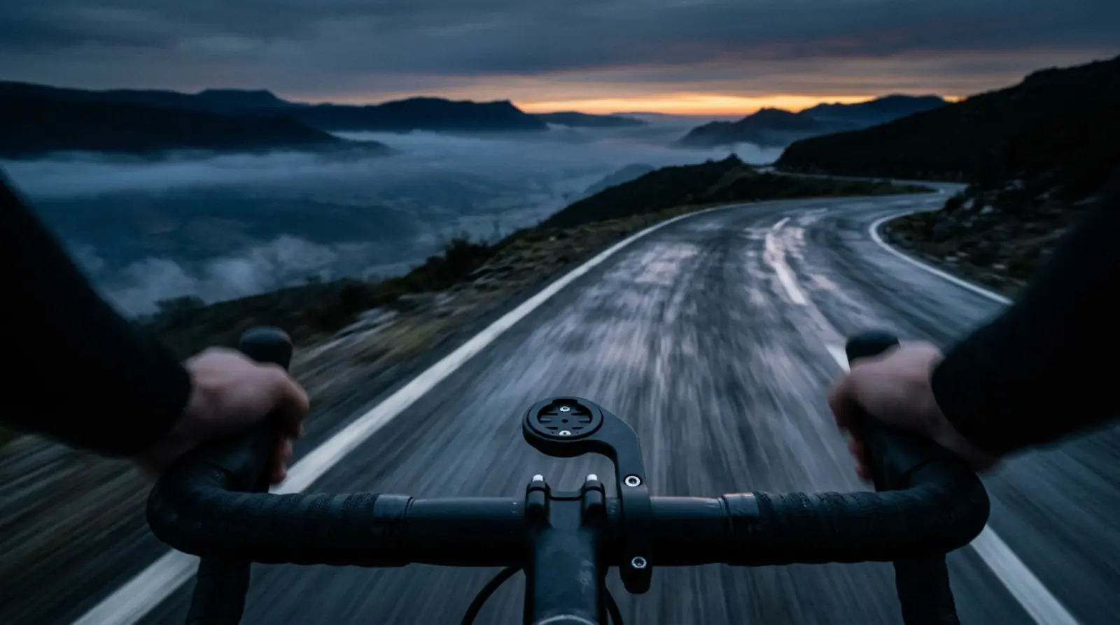 View over the handlebars of a road bike at dawn, on a wet mountain road.